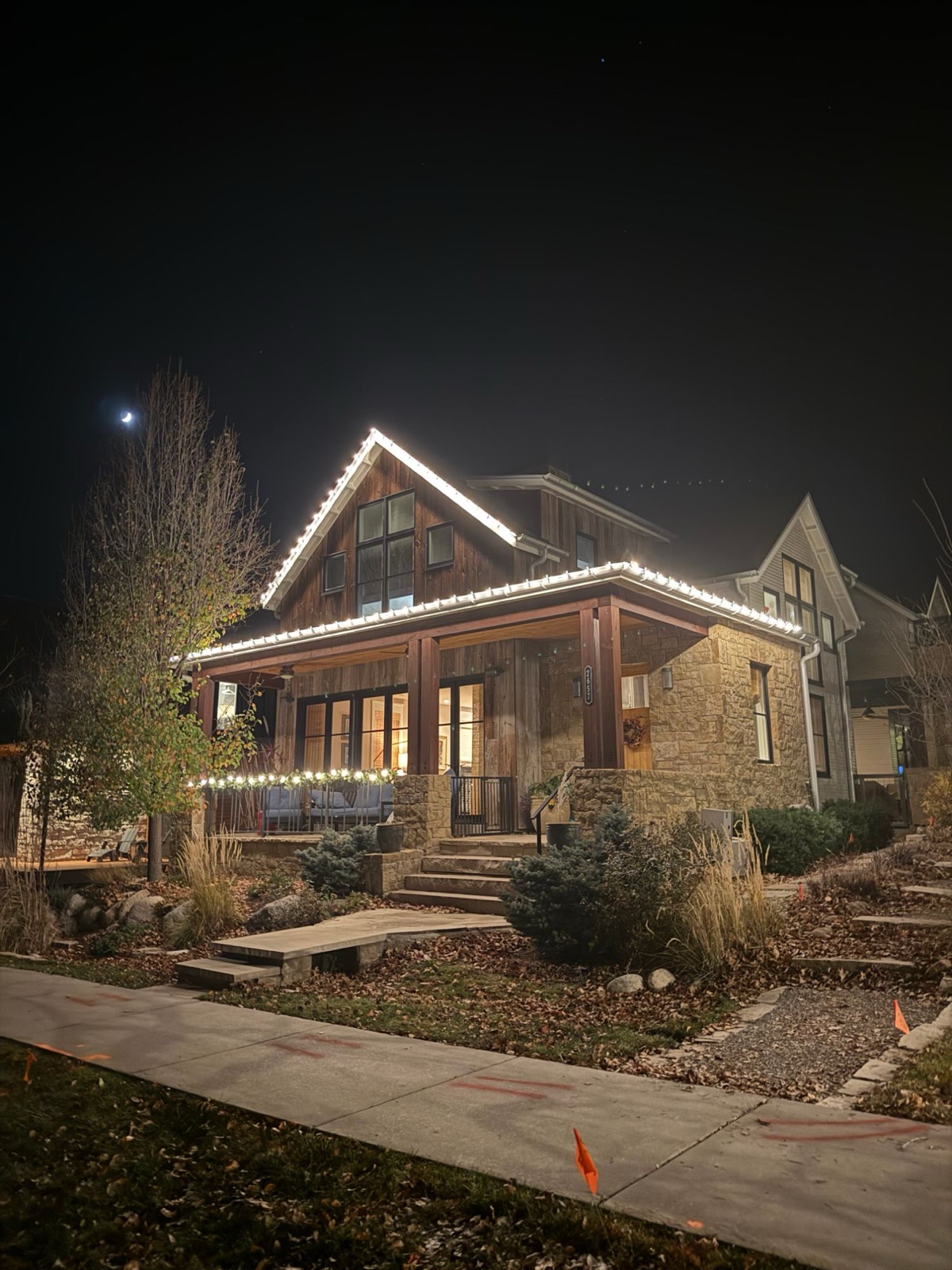 A Boulder County home lit with warm white Christmas lights along the roofline and porch at night